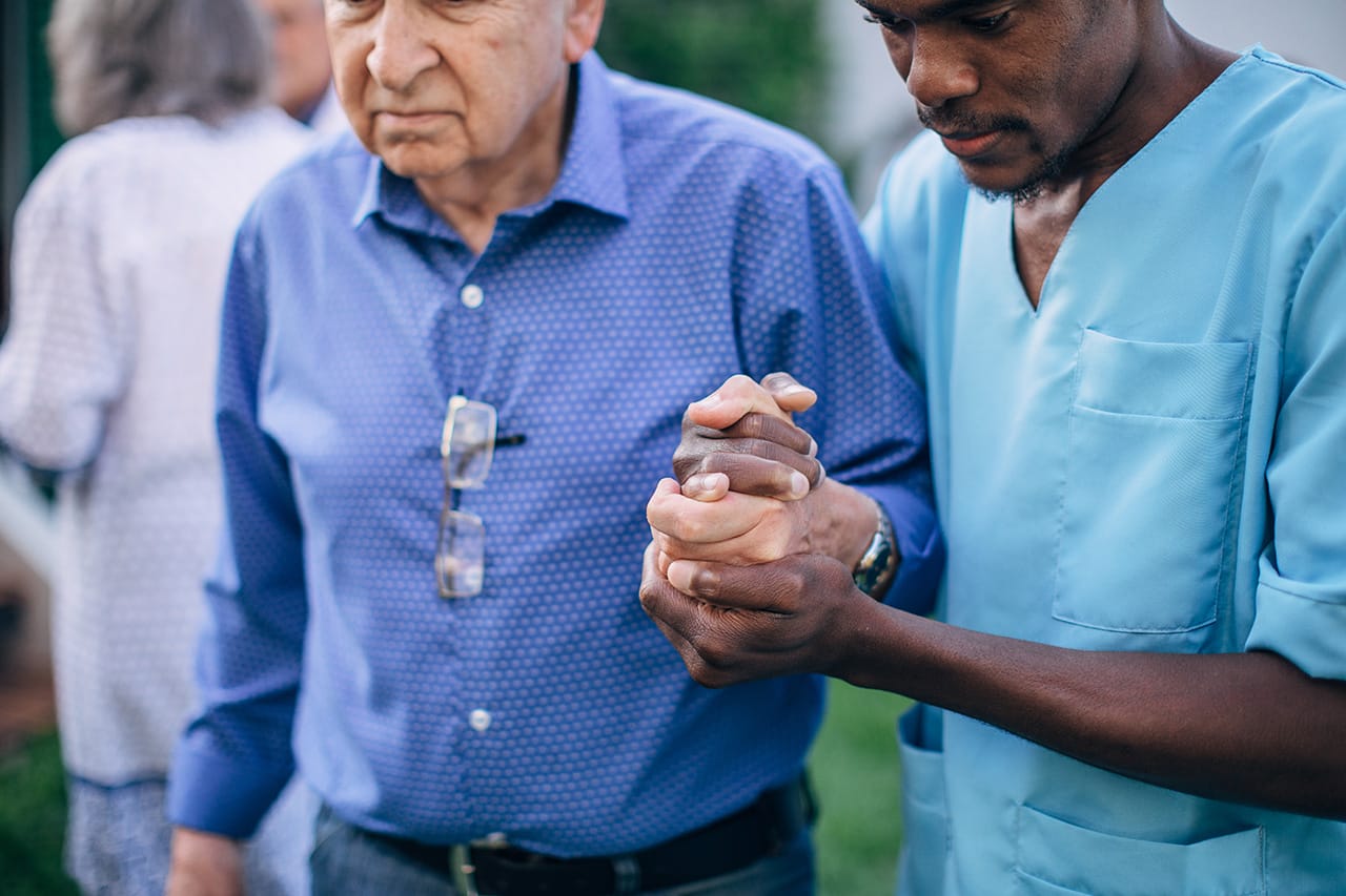 An older man receiving senior home care services in Hallandale Beach, FL holds the hand of his caregiver as they go for a walk.