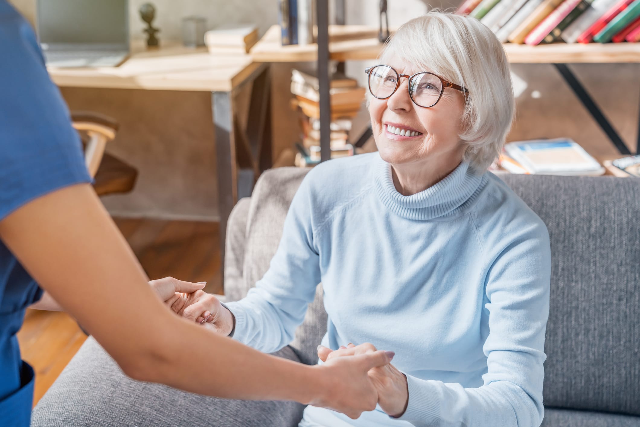 An older woman receiving senior home care services in Tamarac, FL smiles as her caregiver holds her hands to help her stand up.
