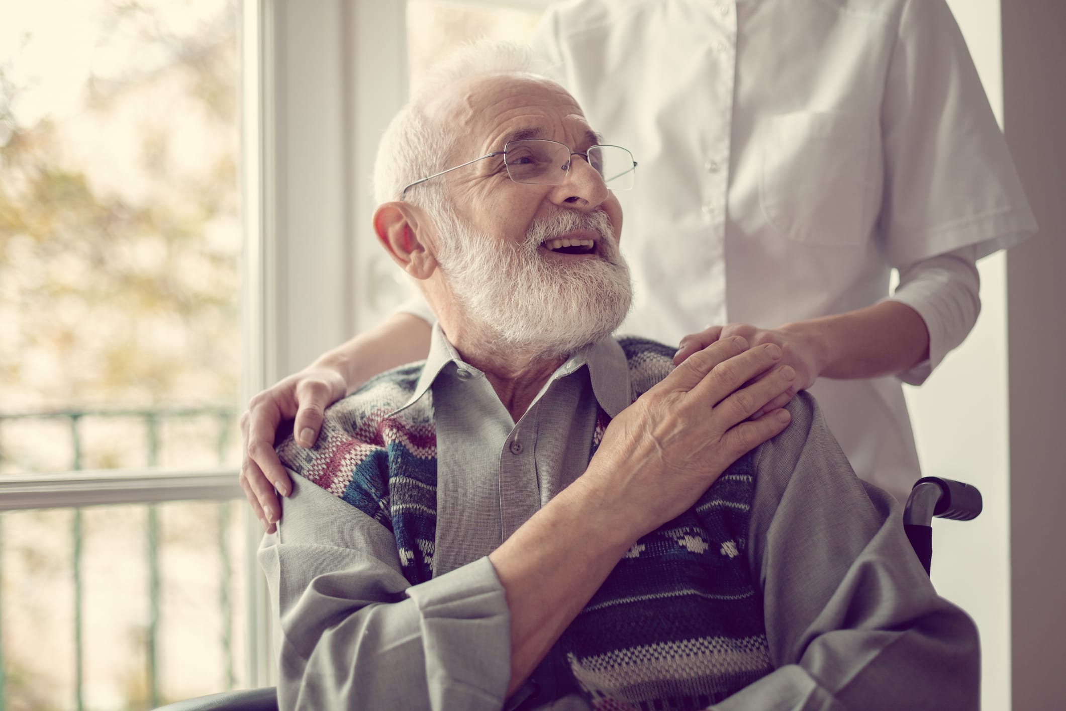 Senior man sitting on the wheelchair, laughing and holding his nurse's hand