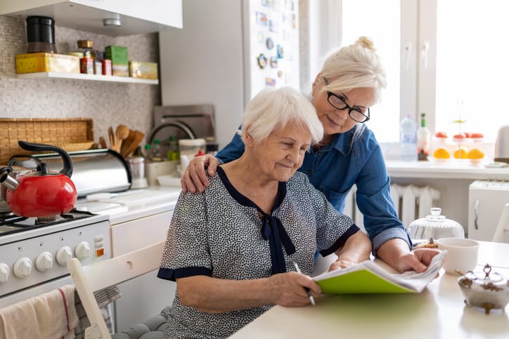 An older woman receiving home care in Coral Springs looks over a recipe with her caregiver in the kitchen.