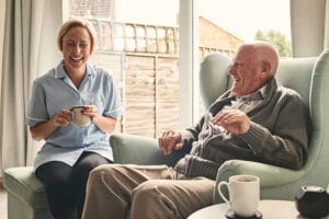 smiling senior man and female carer enjoying coffee in living room