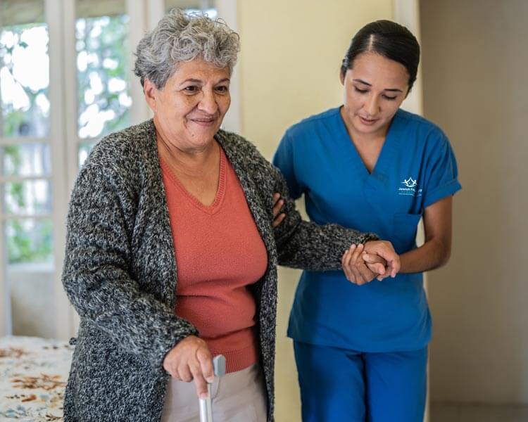 Female client walks with a cane while caregiver assists