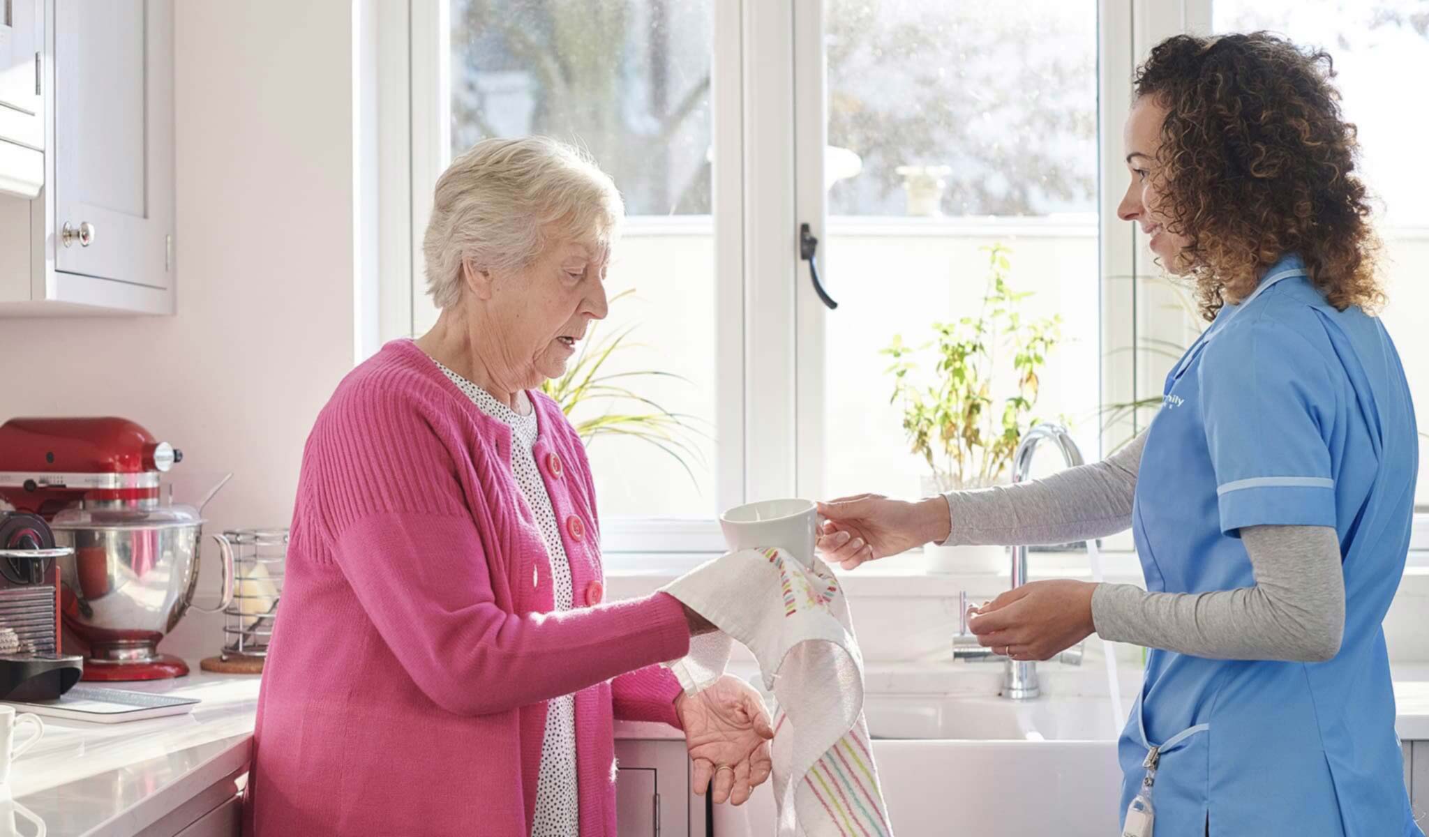 Senior client and caregiver drying dishes in the kitchen