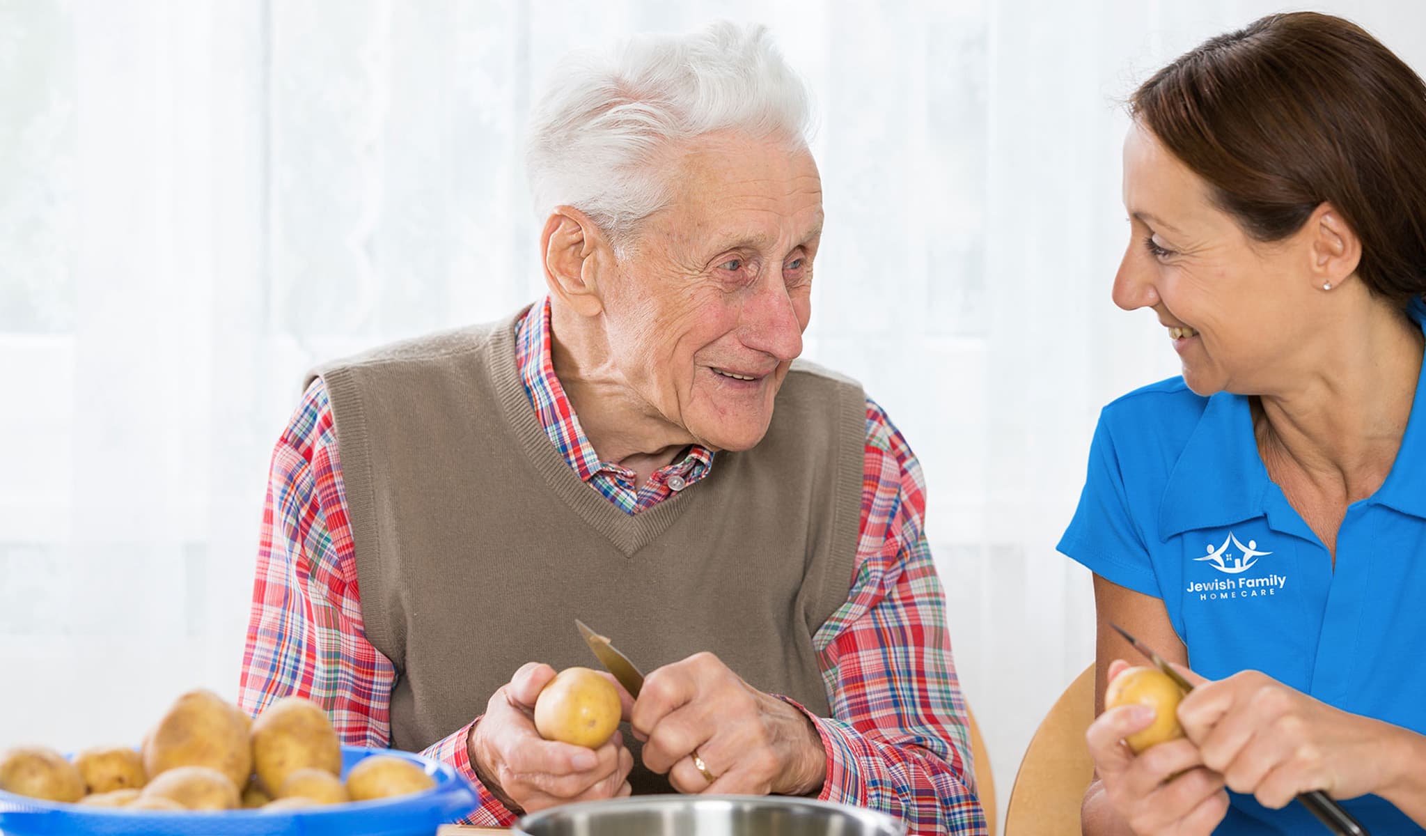 Senior client peeling potatoes with his caregiver
