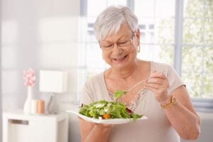 A senior woman eats a salad as she takes steps to overcome senior nutritional hurdles.