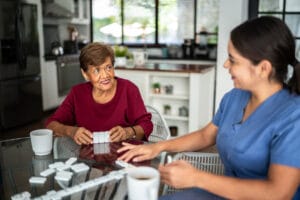 A senior woman feels she’s made the right choice between home care vs. assisted living as she spends time playing dominoes with her caregiver in her own home.