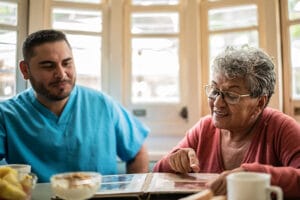 A senior woman shares stories with a caregiver while looking through a photo album, one of the key social benefits of home care.