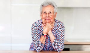 A senior woman smiles, knowing she can access her emergency medical alert system to call for help if needed.