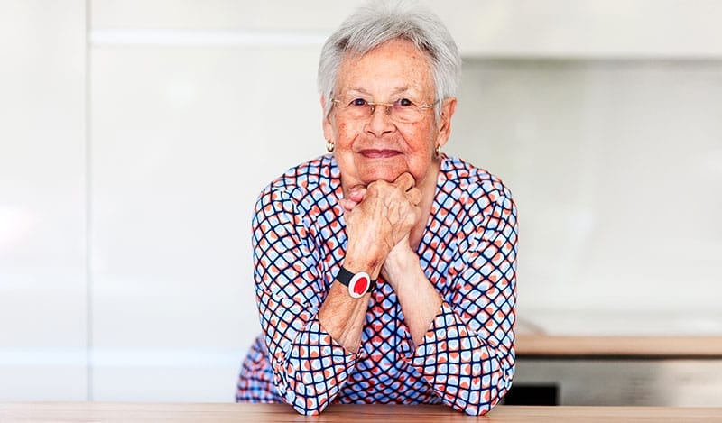 A senior woman smiles, knowing she can access her emergency medical alert system to call for help if needed.