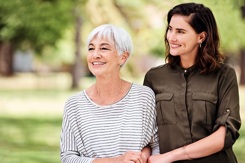 A caregiver helping an older woman with aging in place safely links arms with her as they go for a walk.