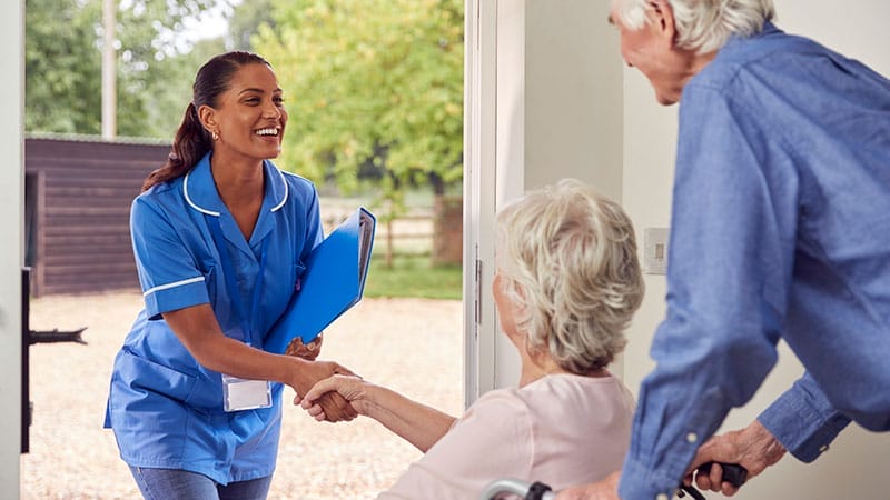 A caregiver smiles and shakes hands with her new clients who are nervous about transitioning to home care services.
