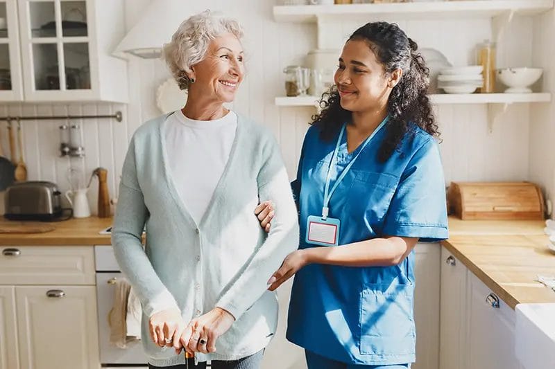 happy older lady and her caregiver standing in kitchen looking at each other