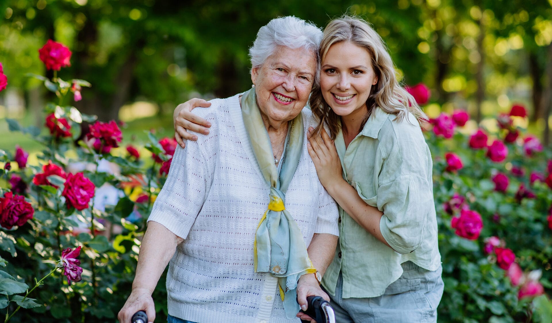 senior landy and her caregiver posing for photo in rose garden